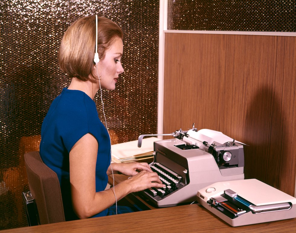 UNITED STATES - Circa 1960s: Woman Secretary Typing Typewriter Listening To Dictation On Tape Recorder Earphones Headset Desk. (Photo by H. Armstrong Roberts/Retrofile/Getty Images)
