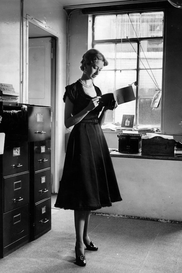 19th August 1950: A woman wearing a black satin dress by Brenner with baby lace around the sleeves, neck and hemline which is not really suitable for the office. Original Publication: Picture Post - 5101 - Four That Are Wrong And One That Is Right - pub. 1950 (Photo by Lee Miller/Picture Post/Getty Images)